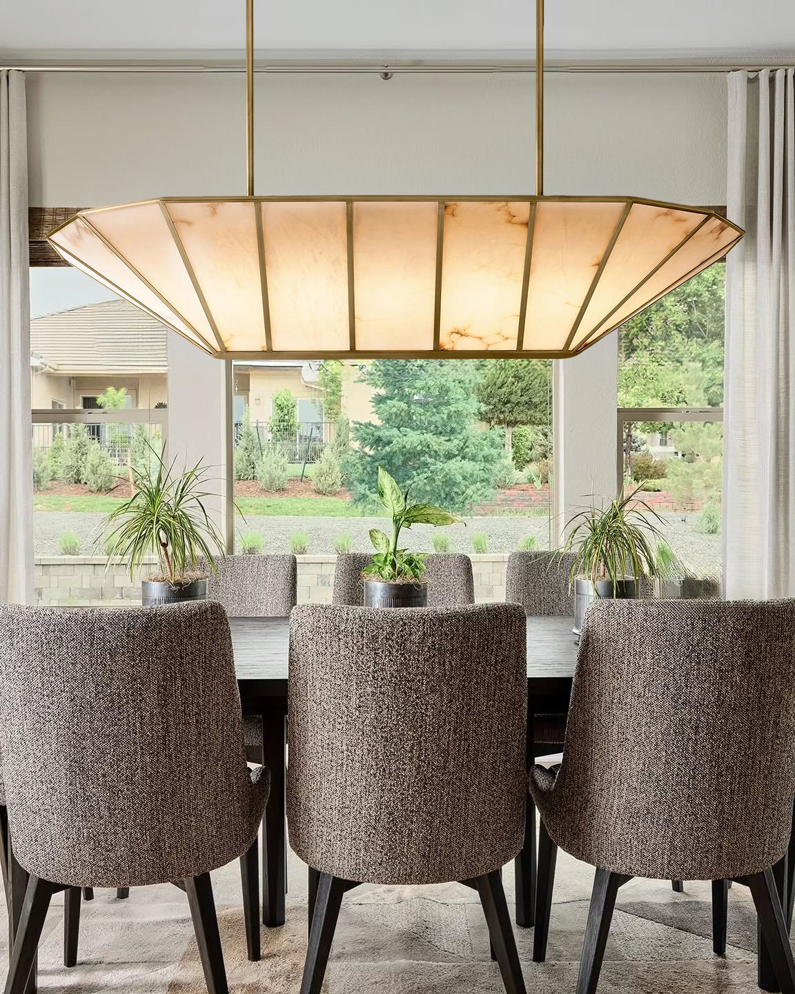 Dining room with a large pendant light fixture, chairs, and a view of greenery outside.